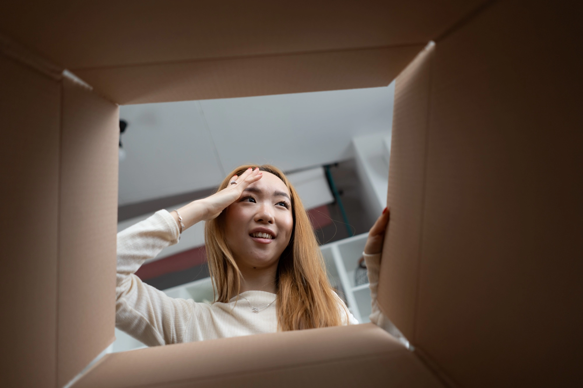 Young Woman Peeking Inside Cardboard Box With Curiosity