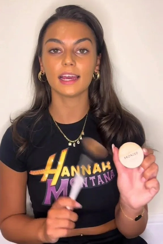 Woman holding bronzer and makeup brush.