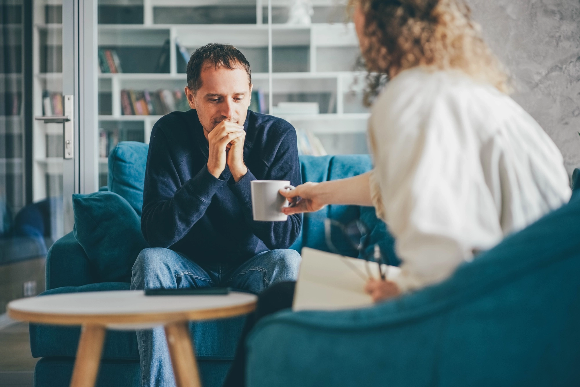 Curly haired woman consultant offers cup of coffee to stressed man client