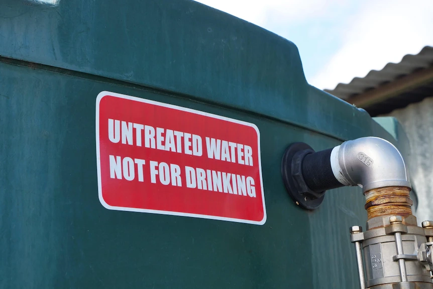 A green water tank with a red sign saying 'untreated water not for drinking'
