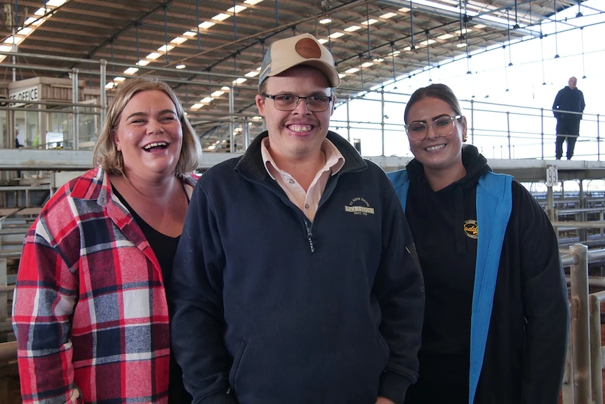Three people inside a livestock saleyard looking at the camera