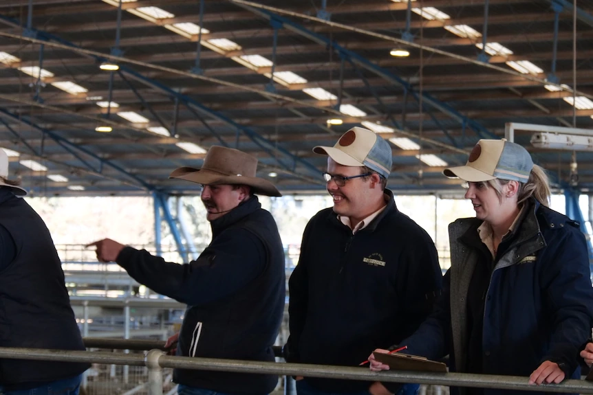 Three people standing behind metal rails in a shed.