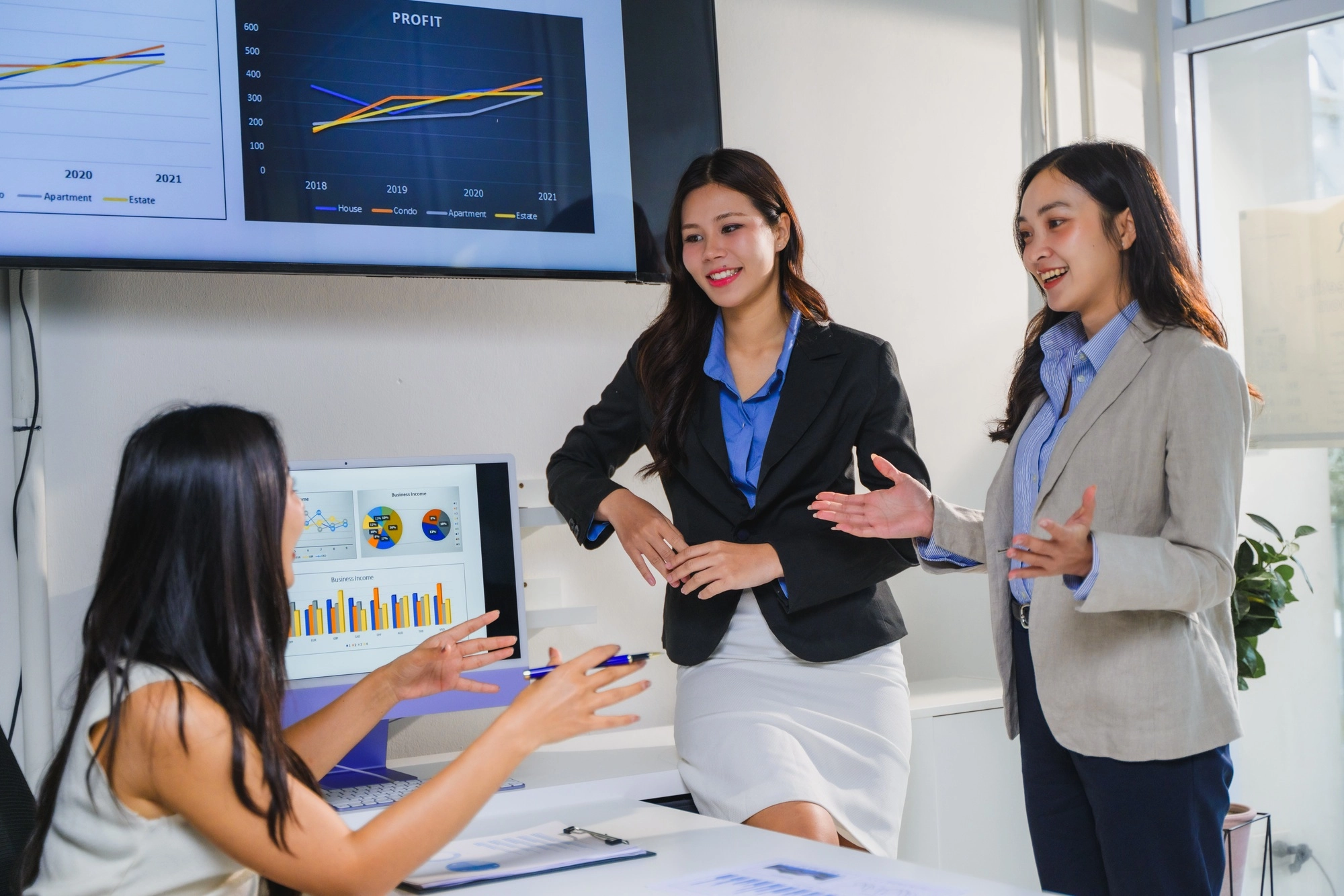 Businesswomen discussing marketing strategy using computer and monitor showing charts