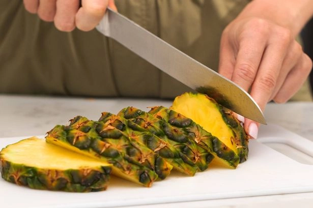 Woman cutting ripe pineapple in kitchen. Tropical fruit concept